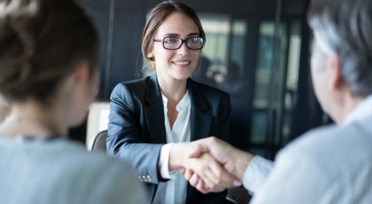 Image shows a financial advisor meeting with clients. A financial advisor who charges a flat hourly or project fee may work with small account holders.