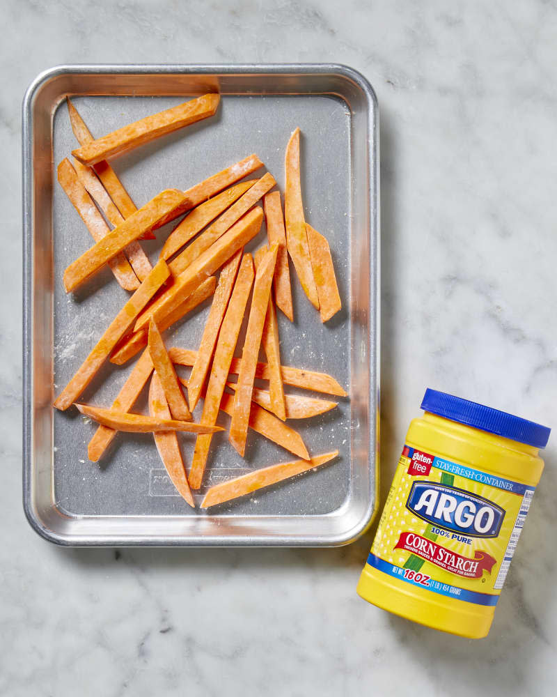 Overhead view of raw sweet potatoes covered in corn starch on a baking sheet.