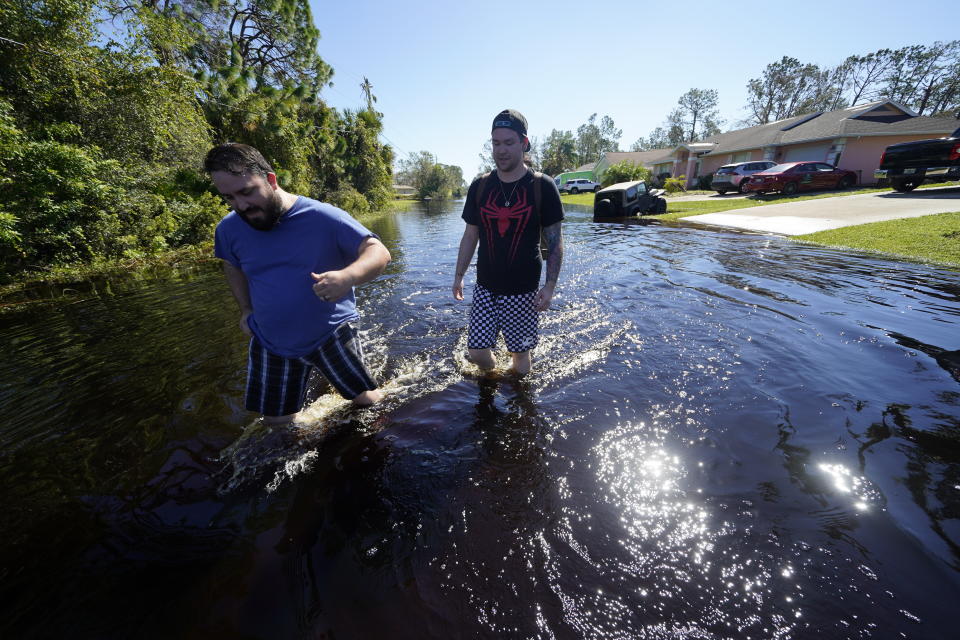 William Merman, left, and his friend Leaf Connor walk through floodwater in Connor's neighborhood in the aftermath of Hurricane Ian in North Port, Fla., Monday, Oct. 3, 2022. (AP Photo/Gerald Herbert)