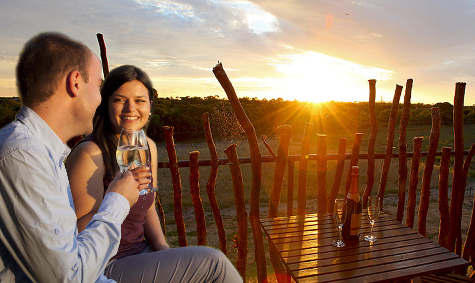 Man and woman smile as they enjoy bubbles as the sun goes down on a deck. Overnight Zoo Safari, $690 for two people