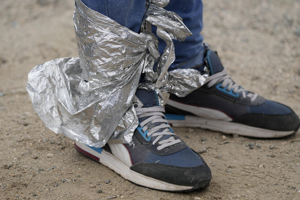 A man from Colombia uses metallic fabric to keep his feet warm as he waits to apply for asylum after crossing the border from Mexico on Wednesday, May 10, 2023, near Jacumba, Calif. The Biden administration on Thursday will begin denying asylum to migrants who arrive at the U.S.-Mexico border without first applying online or seeking protection in a country they passed through, marking a fundamental shift in immigration policy as the U.S. readies for the end of a key pandemic restriction. (AP Photo/Gregory Bull)