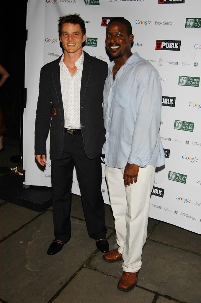 Two men in semiformal attire at an event, both smiling. One in a blazer and shirt, the other in a linen shirt and pants