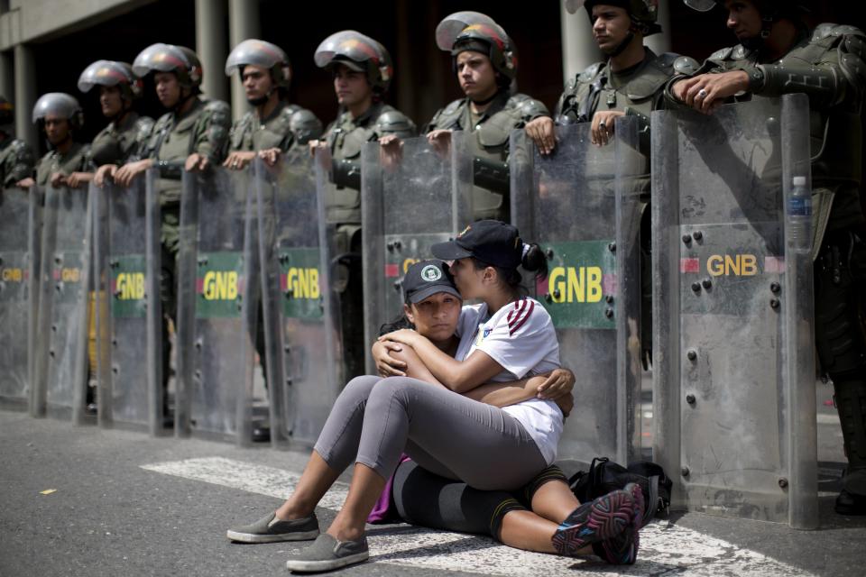 Women embrace as they sit in front of a line of National Bolivarian Guard outside the Palace of Justice court in Caracas, Venezuela, Wednesday, Feb. 19, 2014. Following a dramatic surrender and a night in jail, Venezuelan opposition leader Leopoldo Lopez was due in court Wednesday to learn what charges he may face for allegedly provoking violence during protests against the socialist government in the divided nation. (AP Photo/Rodrigo Abd)