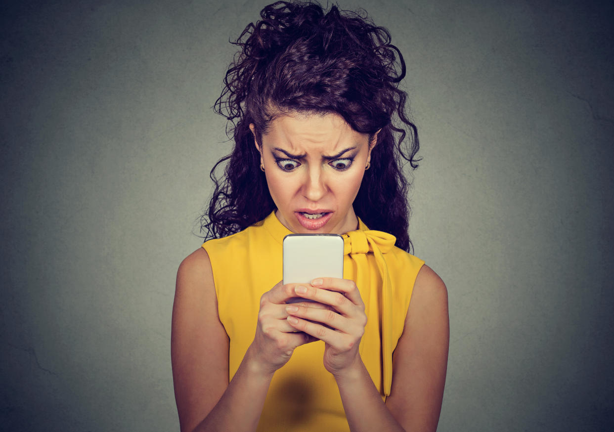 Portrait anxious scared girl looking at phone seeing bad message isolated on gray wall background. Human emotions