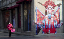 A woman wears a mask as she strolls through a quiet retail street in Beijing, China on Wednesday, Feb. 19, 2020. Even as authorities went door to door to find the infected in Wuhan, the epic center of the viral outbreak, Beijing was showing signs of coming back to life this week, with road traffic at around a quarter of usual, up from virtually nothing a week ago. While most restaurants, stores and office buildings remained closed, others had reopened. (AP Photo/Sam McNeil)