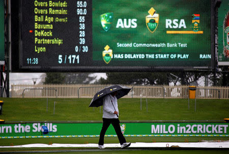 Cricket - Australia v South Africa - Second Test cricket match - Bellerive Oval, Hobart, Australia - 13/11/16 Umpire Mick Martell holds an umbrella while walking around the covered pitch as rain falls during the second day of the second test between Australia and South Africa. REUTERS/David Gray