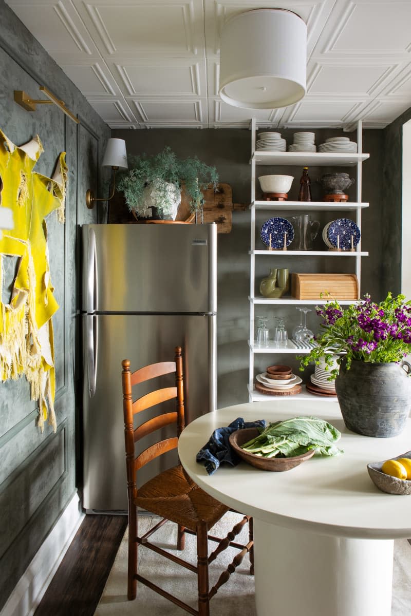 dining area with white round table, refrigerator, and tall shelves with dishes and glassware