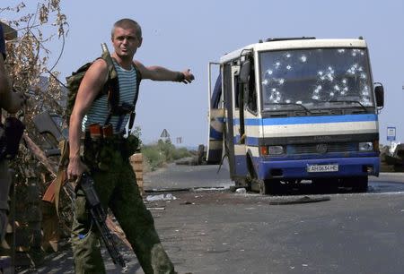 An armed pro-Russian separatist points at a bus riddled with bullet holes at a checkpoint on the outskirts of Donetsk, August 13, 2014. Twelve Ukrainian nationalist fighters, battling a pro-Russian insurgency in eastern Ukraine, were killed early on Wednesday and an unknown number taken captive when rebels ambushed their bus, a spokesman for their group said. REUTERS/Sergei Karpukhin