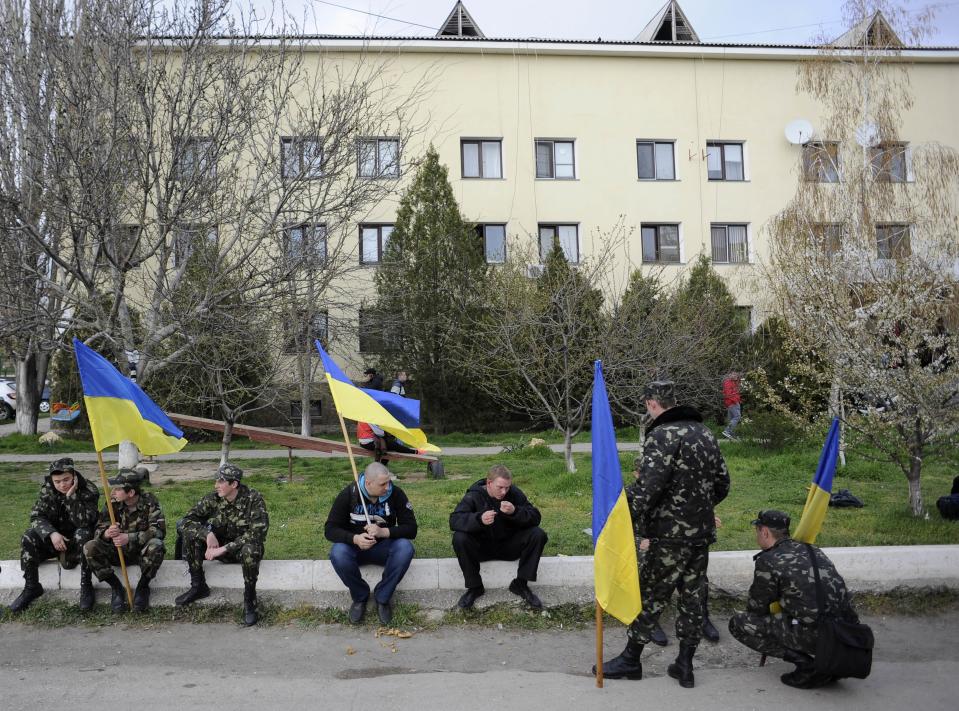 Ukrainian servicemen hold Ukrainian flags as they wait to leave the Belbek airbase near Sevastopol, Crimea, Friday, March 28, 2014. Ukraine started withdrawing its troops and weapons from Crimea, now controlled by Russia. Russia's president says Ukraine could regain some arms and equipment of military units in Crimea that did not switch their loyalty to Russia. (AP Photo/Andrew Lubimov)