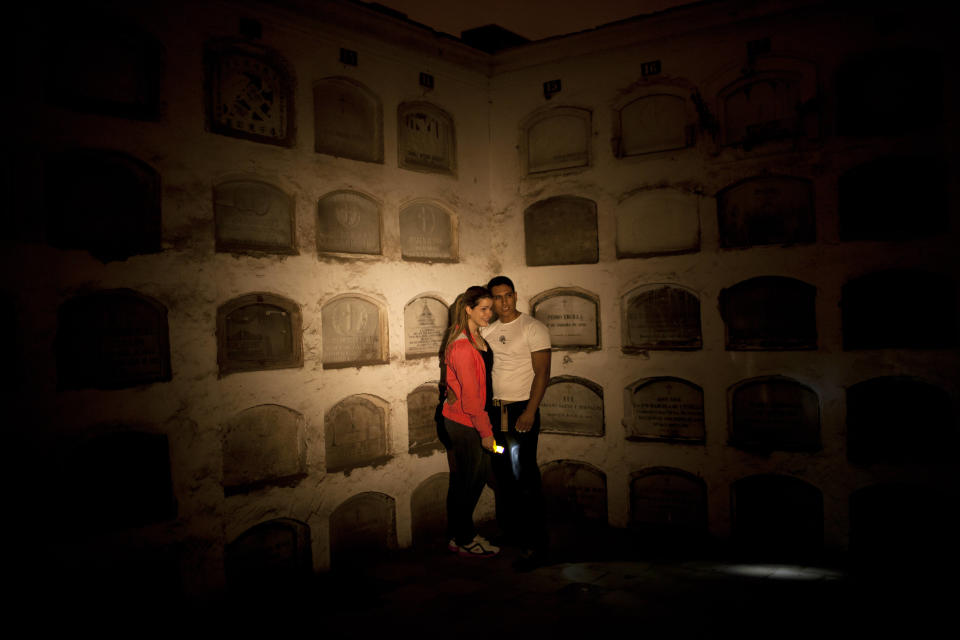 In this Dec. 6, 2012 photo, a couple poses for the picture in front of niches as they take the nighttime guided tour at the Presbitero Matias Maestro cemetery in Lima, Peru. Guides tell Peru's history through the tombs of presidents, prelates, poets, potentates and war heroes. (AP Photo/Rodrigo Abd)