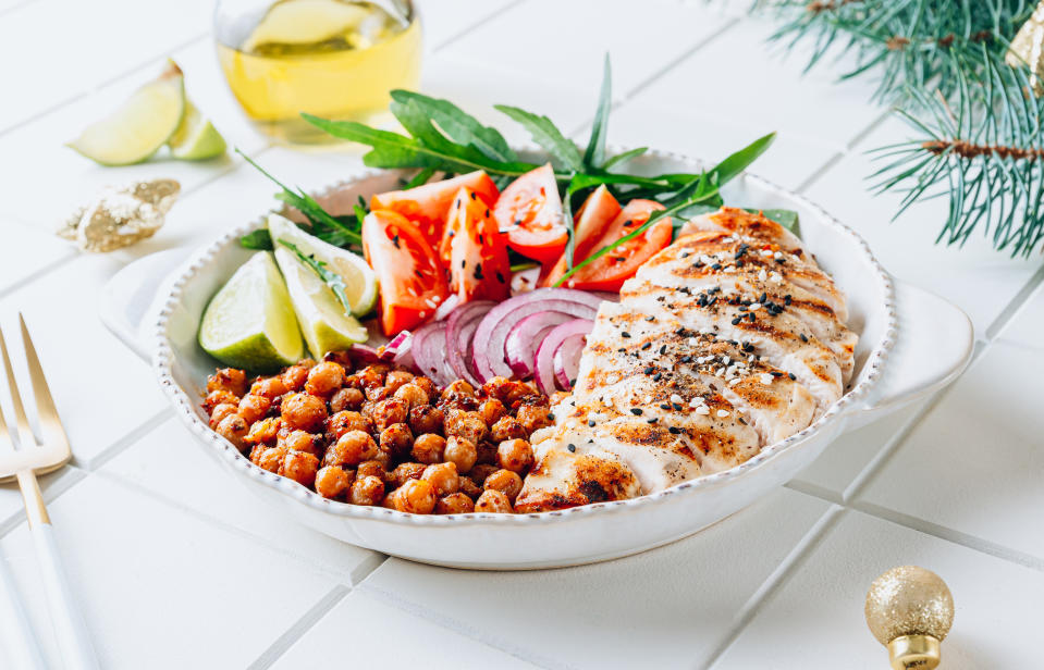 Spicy Chicken Nourish Bowl - A filling and nutritious warm salad with grilled chicken, spicy chickpeas, tomato and arugula on white tile background with Cristmas decor. Balanced food. Selective focus