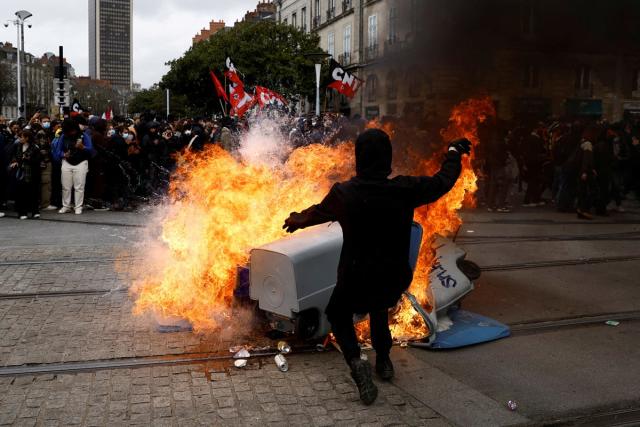 Protesters stand near burning garbage bins during a demonstration as part of the ninth day of nationwide strikes and protests against French government’s pension reform, in Nantes (REUTERS)