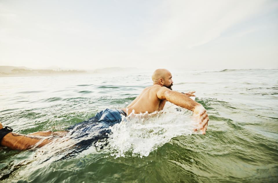 Wide shot of male surfer paddling out in ocean for early morning surf session