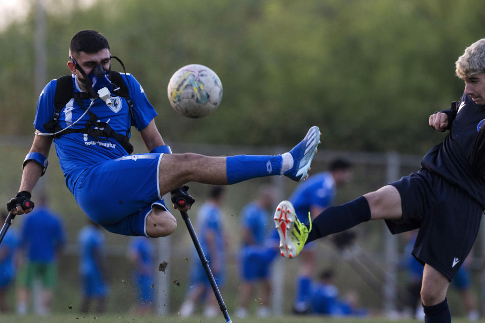 Wearing a device that measures his energy consumption, Israel Amputee Football Team player Ben Maman, left, strikes at a ball against a young soccer player, during a practice session in Ramat Gan, Israel, April 11, 2024. (AP Photo/Leo Correa)