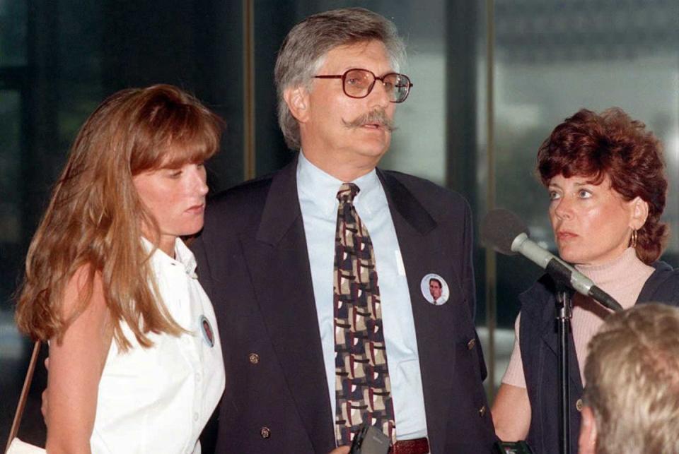 kim goldman, fred goldman, and patti goldman stand together outside a building, fred speaks into a microphone on a stand