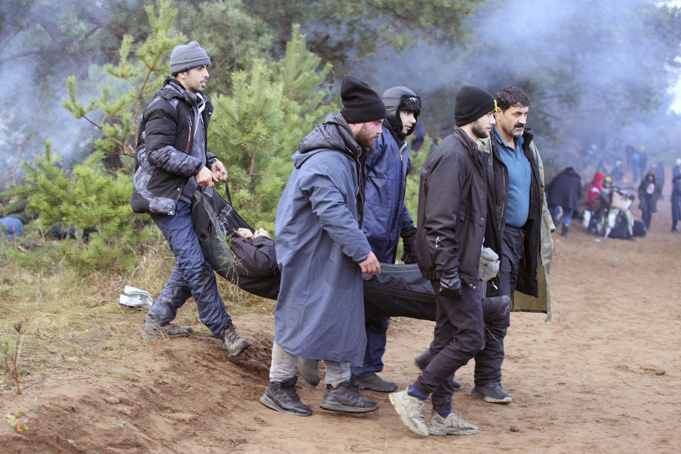 Migrants carry their ill friend as others from the Middle East and elsewhere gather at the Belarus-Poland border near Grodno, Belarus, Monday, Nov. 8, 2021. Poland increased security at its border with Belarus, on the European Union's eastern border, after a large group of migrants in Belarus appeared to be congregating at a crossing point, officials said Monday. The development appeared to signal an escalation of a crisis that has being going on for months in which the autocratic regime of Belarus has encouraged migrants from the Middle East and elsewhere to illegally enter the European Union, at first through Lithuania and Latvia and now primarily through Poland. (Leonid Shcheglov/BelTA via AP)