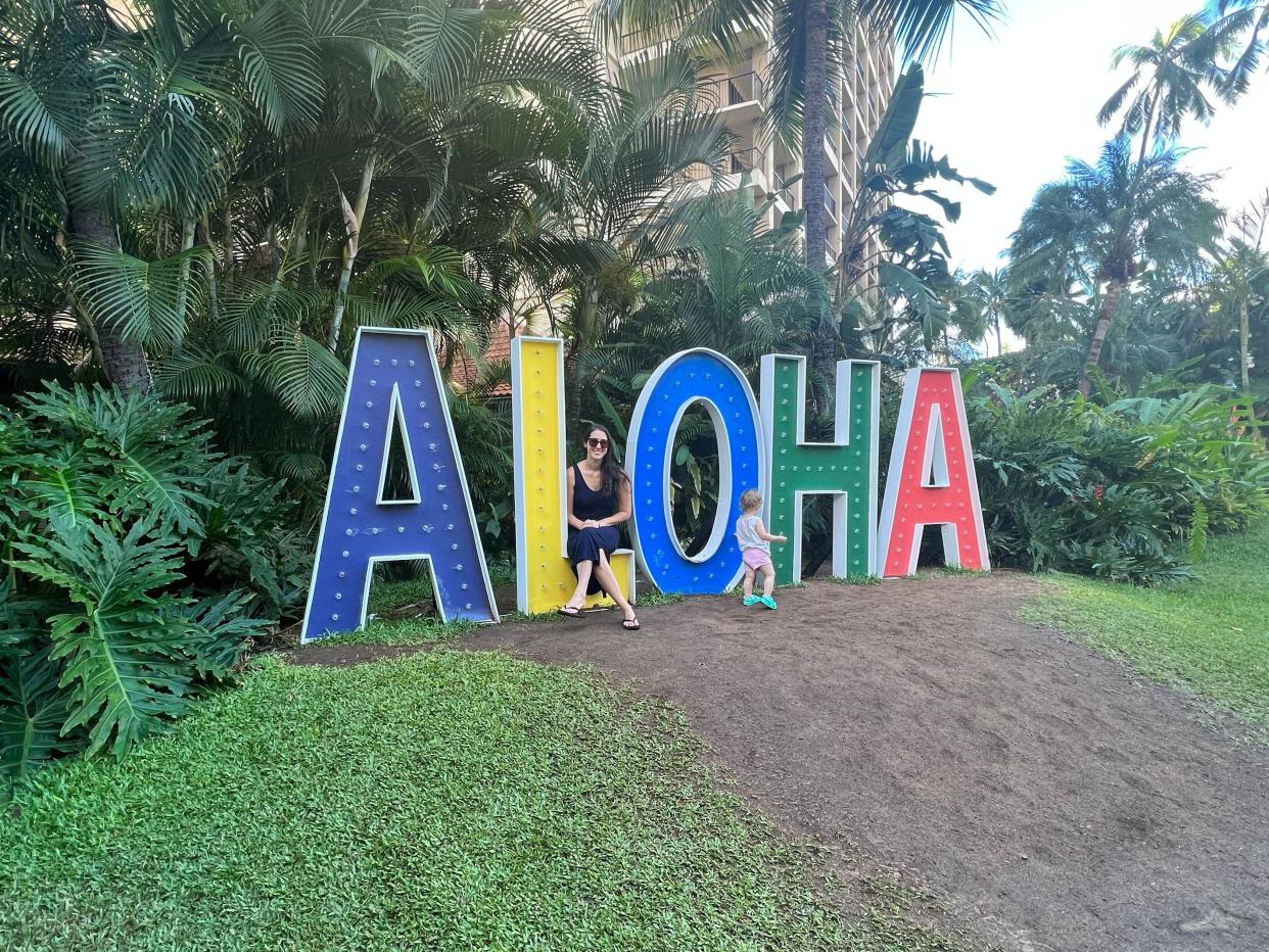 A woman and her child sitting on a lifesize colorful Aloha sign.