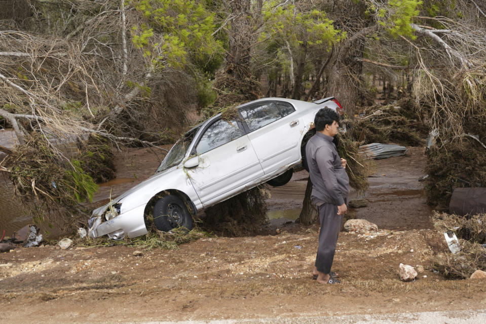 A man stands next to a car that sits partly suspended in trees after being carried by floodwaters in Derna.