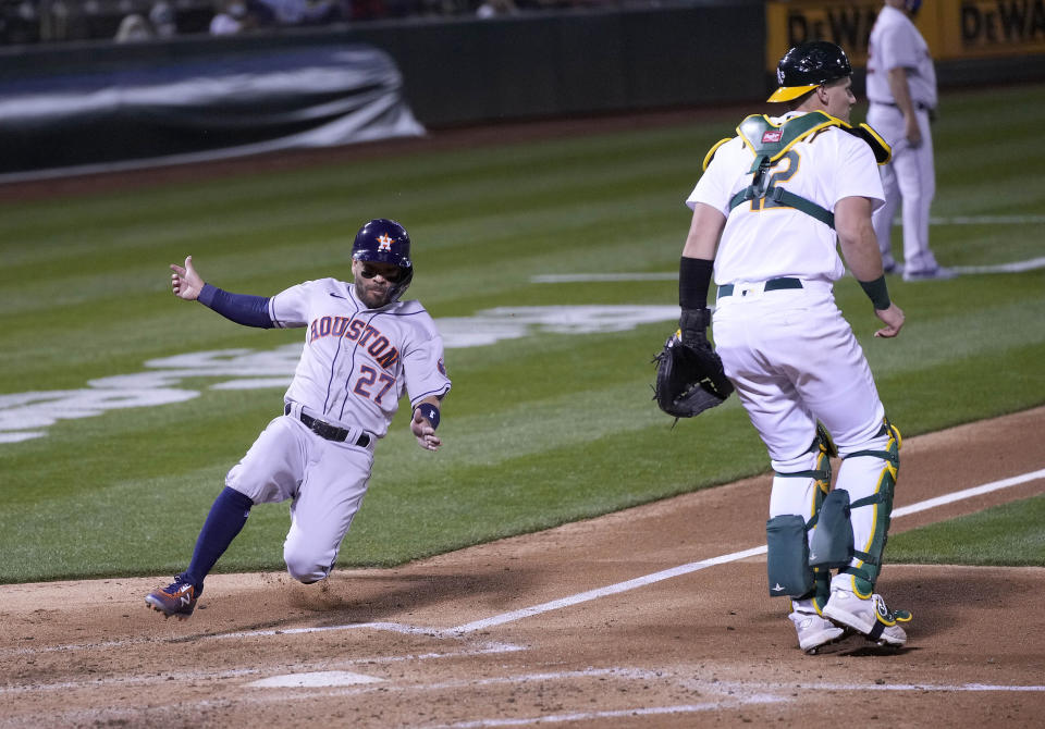 Houston Astros' Jose Altuve (27) slides into home plate past Oakland Athletics catcher Sean Murphy (12) to score a run during the fourth inning of an opening day baseball game Oakland, Calif., Thursday, April 1, 2021. (AP Photo/Tony Avelar)