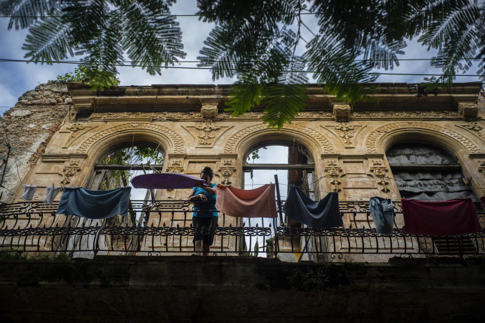 In this Nov. 10, 2019 photo, a woman pulls towels off the line after they dried on the balcony of an old home, missing part of its roof, in Havana, Cuba. The city will celebrate its 500th anniversary on Nov. 16. (AP Photo/Ramon Espinosa)