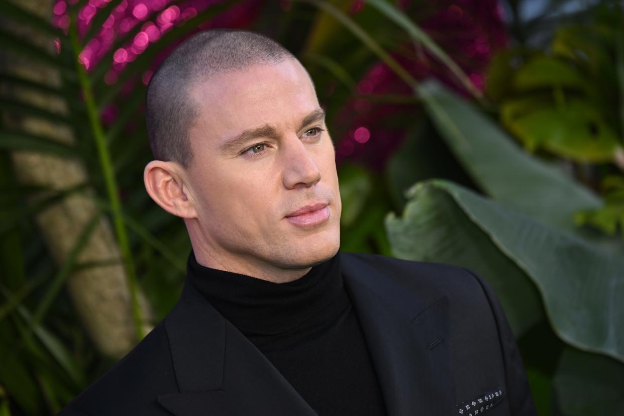 Channing Tatum standing in front of a leafy background in all black