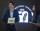 Grand Chief Peter Johnston watches as Canadian Prime Minister Justin Trudeau reacts to being given a framed archival photo of his father Pierre and brother Sasha playing on a swing set in Old Crow, Yukon, back in the early 1970s, at a dinner event during Council of Yukon First Nations' Together Today For Our Children Tomorrow 50th Anniversary celebrations at the Kwanlin Dun Cultural Centre in Whitehorse, Yukon, on Sunday, Feb. 12, 2023. (Mike Thomas/The Canadian Press via AP)