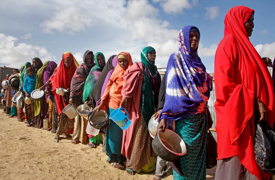 women in colorful cloth line up with buckets pots bowls and jugs