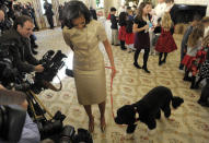 First lady Michelle Obama, accompanied by first dog Bo, walks past reporters during a visit to the State Dining Room of the White House in Washington, Wednesday, Nov. 28, 2012, during a preview of the White House holiday decorations. The theme for the White House Christmas 2012 is Joy to All. School children were also in the State Dining Room decorating holiday treats. (AP Photo/Susan Walsh)