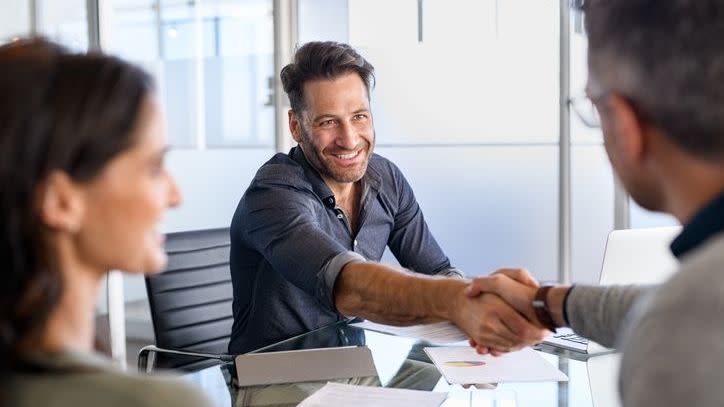 A financial advisor shakes hands with two new clients at the end of their first meeting.