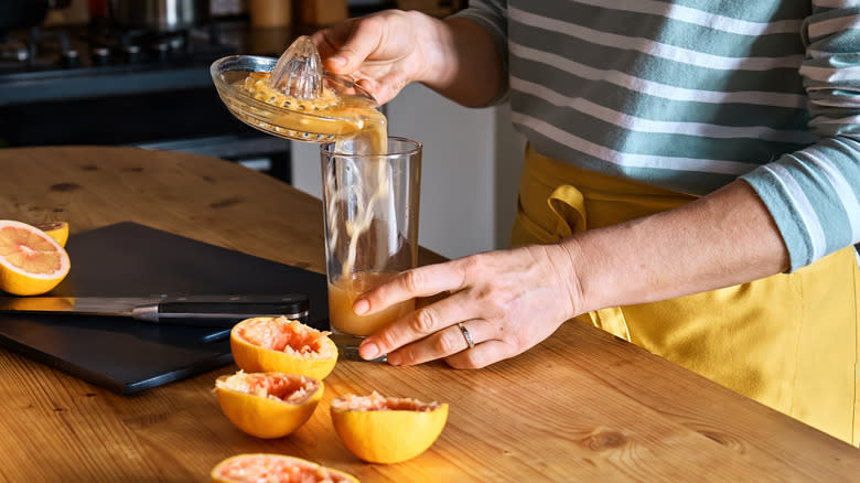 Hands pouring fresh grapefruit juice into a glass
