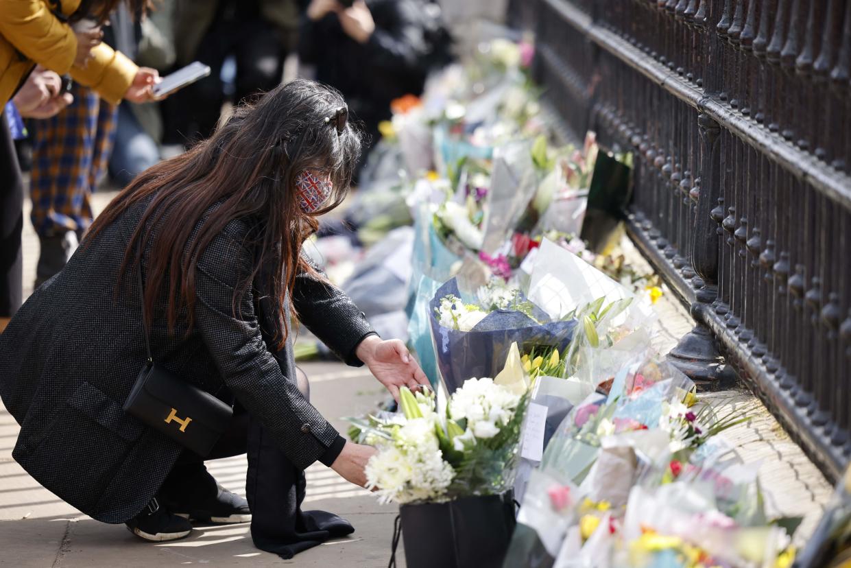 A woman adds a bunch of flowers to a line of floral tributes against the railings at the front of Buckingham Palace in central London on April 9, 2021 after the announcement of the death of Britain's Prince Philip, Duke of Edinburgh. - Queen Elizabeth II's husband Prince Philip, who recently spent more than a month in hospital and underwent a heart procedure, died on April 9, 2021, Buckingham Palace announced. He was 99. (Photo by Tolga Akmen / AFP) (Photo by TOLGA AKMEN/AFP via Getty Images)