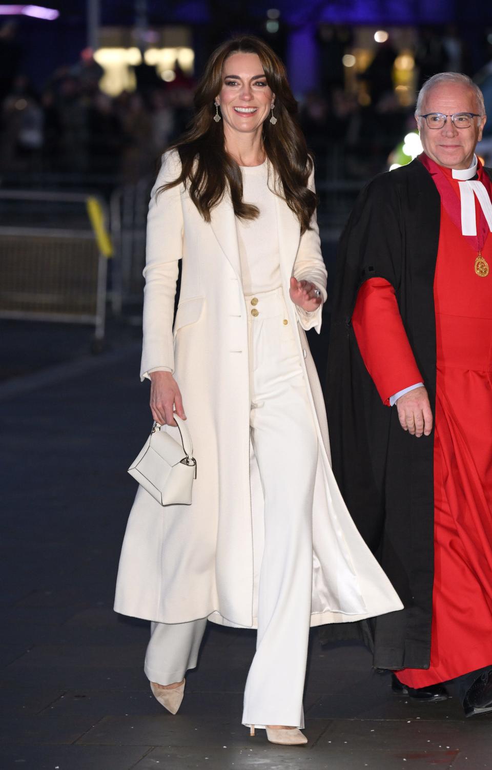 Kate Middleton walks in a white top, white jeans, and a white jacket.