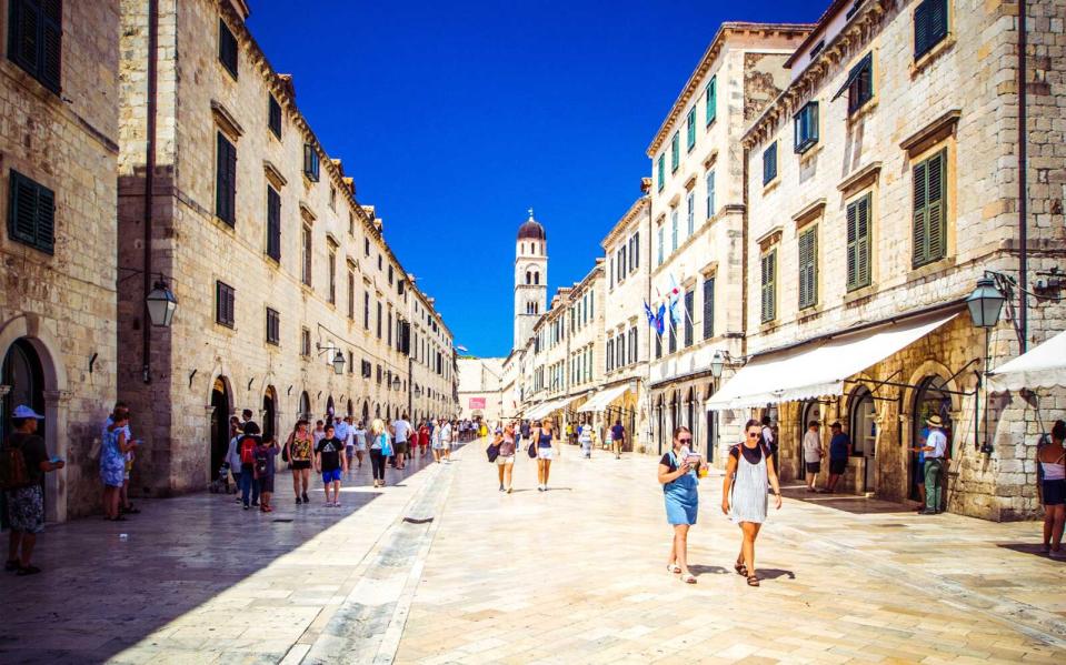 Tourists walk along paved stone streets of old city of Dubrovnik on warm sunny day, Dubrovnik, Croatia.