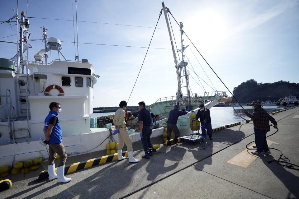 Paul McGinnity, left, research scientist of the International Atomic Energy Agency (IAEA) observes a fishing boat unloading catch of the day for a morning auction at Hisanohama Port in Iwaki, northeastern Japan Thursday, Oct. 19, 2023. They are visiting Fukushima for its first marine sampling mission since the Fukushima Daiichi nuclear power plant started releasing the treated radioactive wastewater into the sea. (AP Photo/Eugene Hoshiko, Pool)