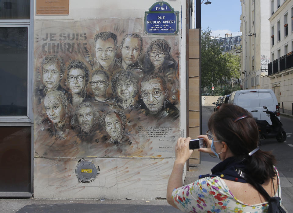 A woman wearing a protective face mask as a precaution against the coronavirus takes a pictures of a painting by French street artist Christian Guemy, a.k.a. 'C215' in Paris Wednesday, Sept. 2, 2020, in tribute to the members of the satirical newspaper Charlie Hebdo attack by jihadist gunmen in January 2015. Thirteen men and a woman go on trial Wednesday over the 2015 attacks against a satirical newspaper and a kosher supermarket in Paris that marked the beginning of a wave of violence by the Islamic State group in Europe. Seventeen people and all three gunmen died during the three days of attacks in January 2015. (AP Photo/Michel Euler)