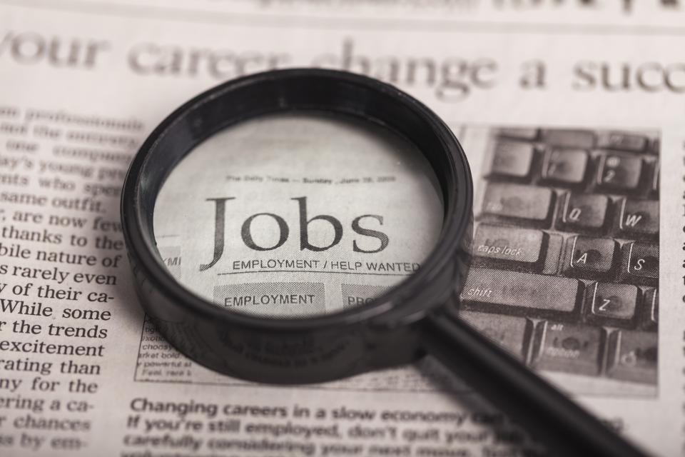 A magnifying glass rests on a newspaper jobs advert. (Source: Getty)