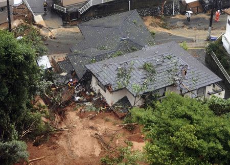 Rescue workers are seen next to houses damaged by a landslide following heavy rain in Kitakyushu, southwestern Japan, in this photo taken by Kyodo July 6, 2018. Mandatory credit Kyodo/via REUTERS