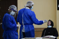 A medical worker collects a swab sample from a woman during coronavirus testing in Petaling Jaya, Malaysia, Monday, Jan. 18, 2021. Malaysian authorities imposed tighter restrictions on movement to try to halt the spread of the coronavirus. (AP Photo/Vincent Thian)