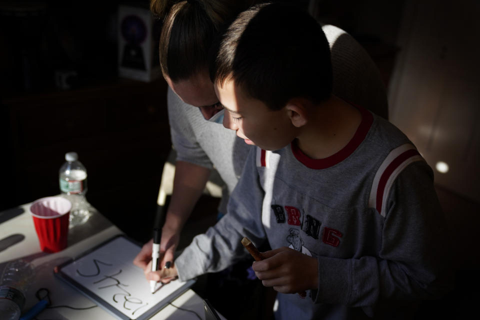 Paraprofessional Jessica Wein helps Josh Nazzaro write numbers while attending class virtually from his home in Wharton, N.J., Wednesday, Nov. 18, 2020. The pandemic is threatening to wipe out the educational progress made by many of the nation’s 7 million students with disabilities. That's according to advocates, who say the extended months of learning from home and erratic attempts to reopen schools are deepening a crisis that began with the switch to distance learning in March. (AP Photo/Seth Wenig)