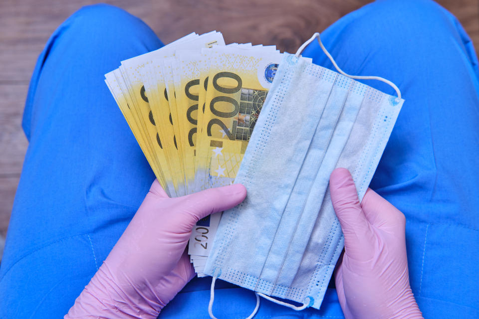 Doctor holds a protective mask and banknotes in his lap. 