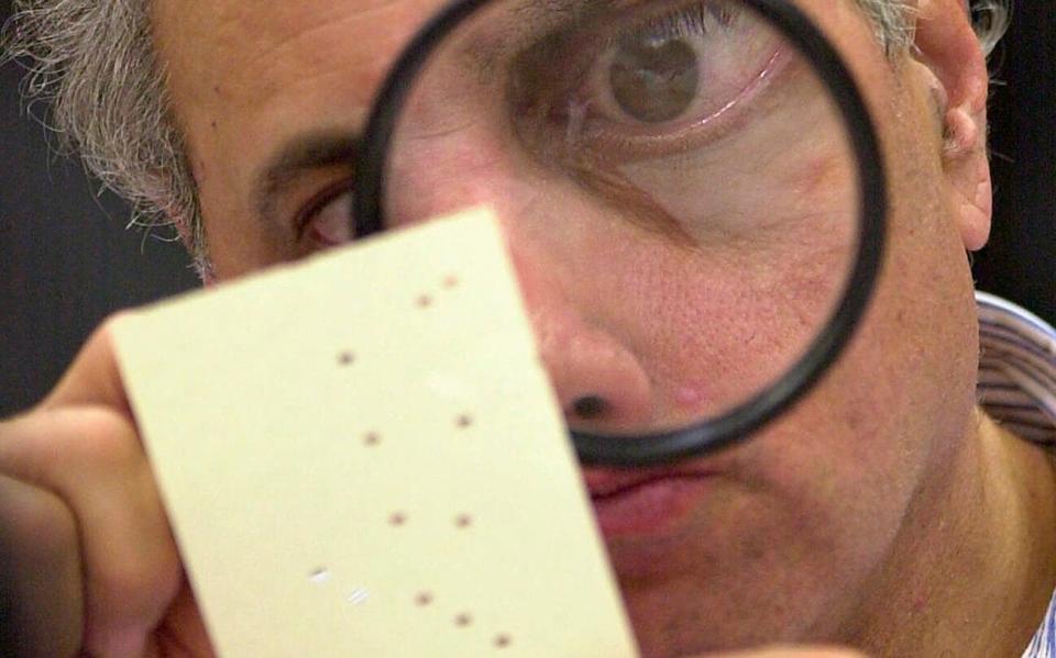 In this Nov. 24, 2000, file photo, Judge Robert Rosenberg uses a magnifying glass to examine a disputed election ballot - Alan Diaz/AP