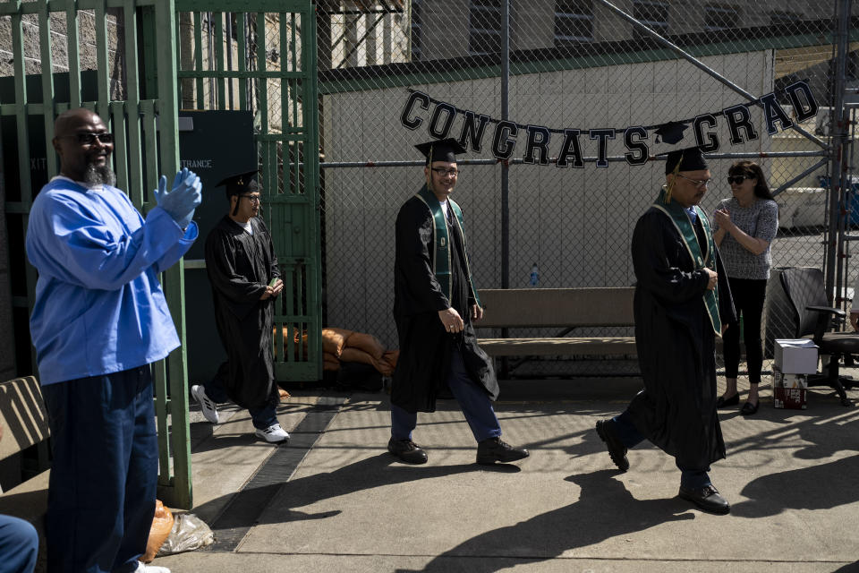 A prisoner applauds as Lambert Pabriaga, right, and Eric Pomatto, center, walk into their graduation ceremony at Folsom State Prison in Folsom, Calif., Thursday, May 25, 2023. Pabriaga and Pomatto earned their bachelor's degrees in communications in prison through the Transforming Outcomes Project at Sacramento State. (AP Photo/Jae C. Hong)