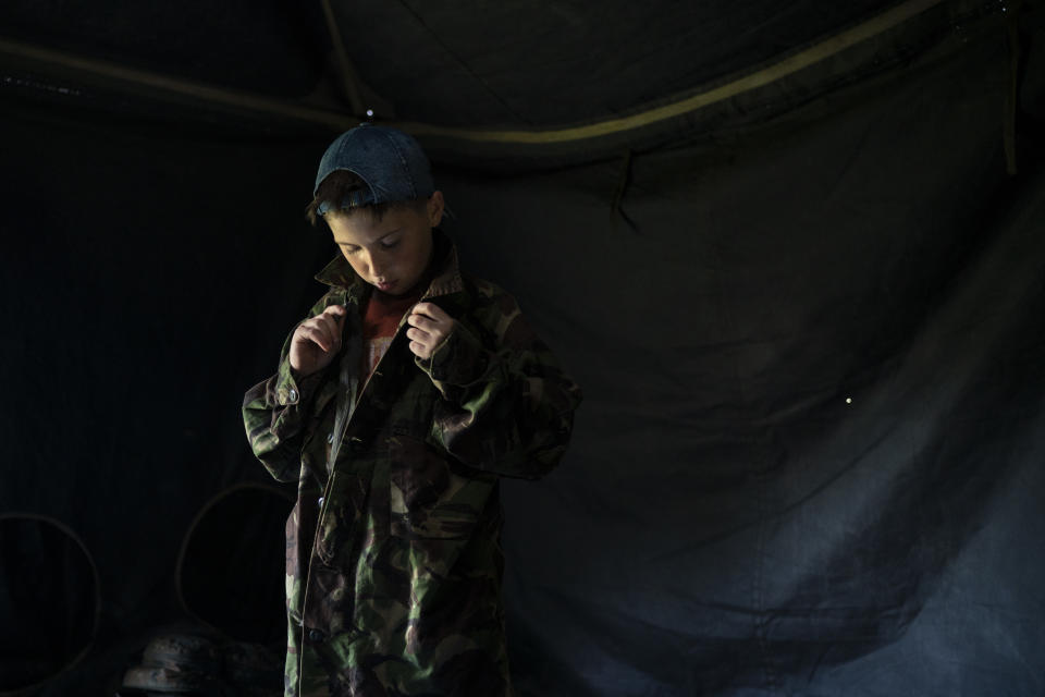 In this July 27, 2018 photo, a young participant of the "Temper of will" summer camp, organized by the nationalist Svoboda party, buttons up a camouflage shirt as he prepares for an exercise in a village near Ternopil, Ukraine. Campers as young as 8 years old practice using assault rifles. They are taught to shoot to kill Russians and their sympathizers. (AP Photo/Felipe Dana)