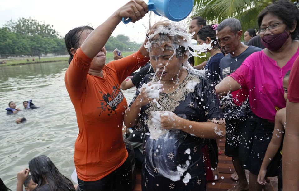 A woman is helped to take shower in the Cisadane River on the first evening of the holy fasting month of Ramadan in Tangerang, Indonesia, Saturday, April 2, 2022. Muslims followed local tradition to wash in the river to symbolically cleanse their soul prior to entering the holiest month in Islamic calendar. (AP Photo/Tatan Syuflana)