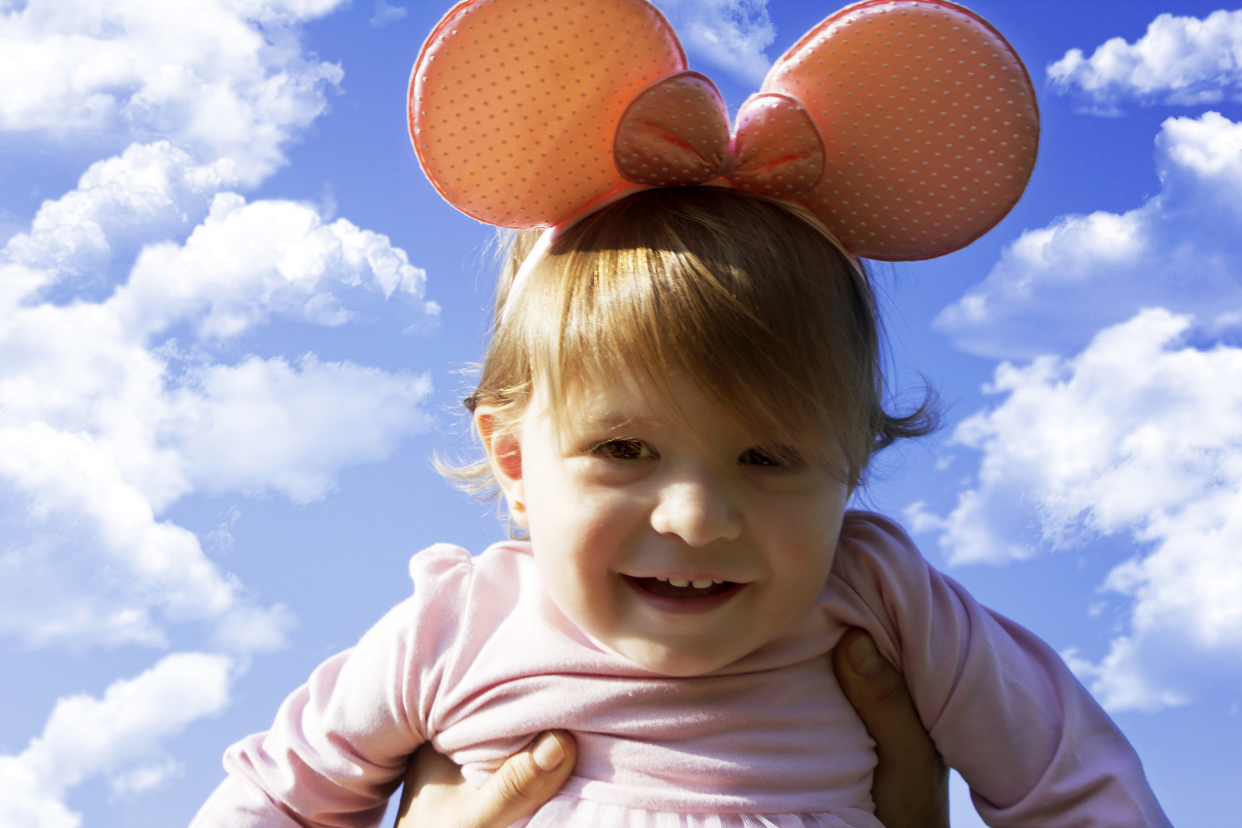 Little girl wearing a Minnie Mouse bow being held up toward the sky