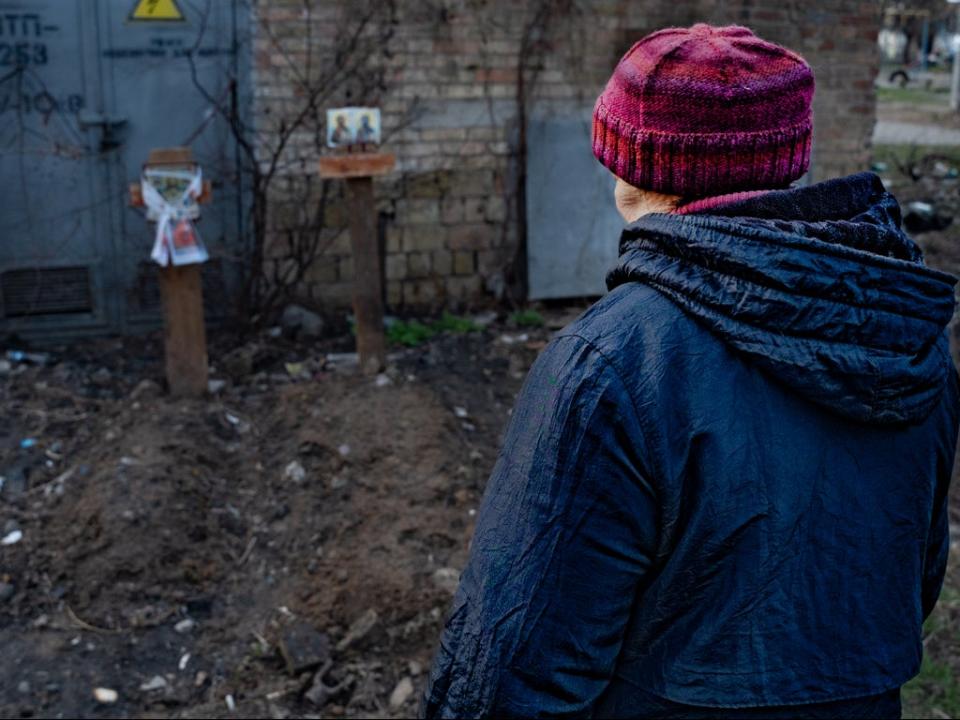 Helena prays by the graves she helped dig outside her flat window in Bucha (Bel Trew)