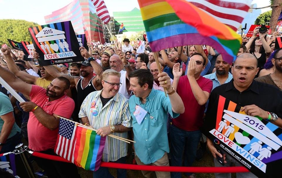 A crowd of people waving Pride flags and the U.S. flag