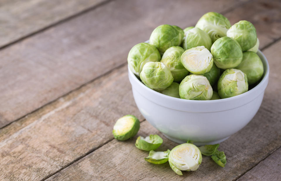 Raw brussels sprouts in white bowl on wooden rustic desk.