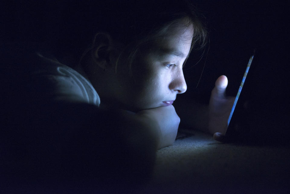 A teenager in the dark, lit by the screen of her smartphone.