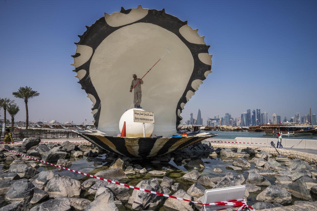 A migrant laborer paints The Pearl Monument, a sculpture depicting an open oyster shell with running water, on the corniche, overlooking the skyline of Doha, Qatar, Wednesday, Oct. 19, 2022. One of the world’s biggest sporting events has thrown an uncomfortable spotlight on Qatar’s labor system, which links workers’ visas to employers and keeps wages low for workers toiling in difficult conditions. (AP Photo/Nariman El-Mofty)